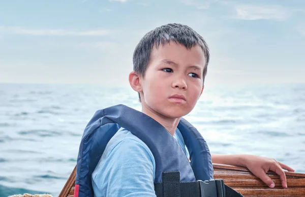 Serious pensive Asian boy in life jacket over background of sea and sky. — Zdjęcie stockowe