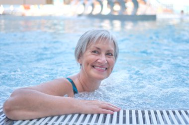 Senior woman with gray hair in outdoor thermal pool with hydromassage. clipart