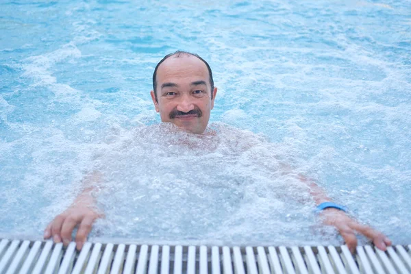 Sonriendo hombre asiático maduro mirando a la cámara en la piscina termal al aire libre con hidromasaje. — Foto de Stock