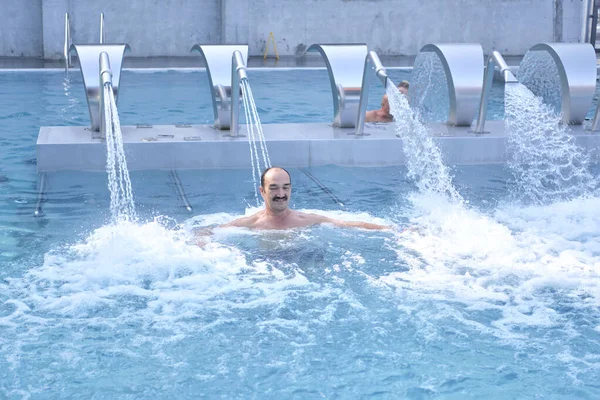 Feliz hombre asiático maduro haciendo masaje con chorros de agua del inyector en la piscina termal al aire libre. — Foto de Stock
