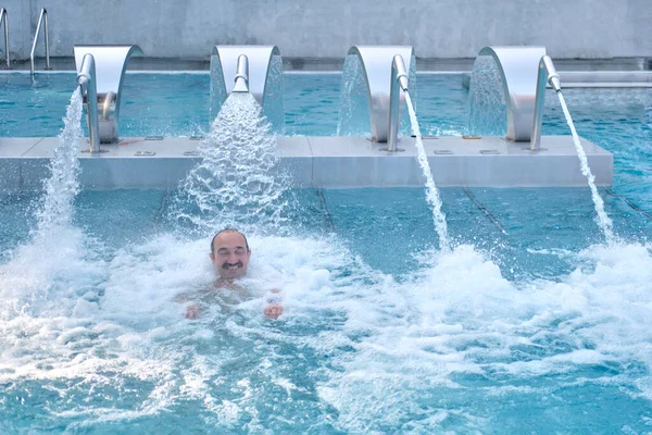 Feliz hombre asiático maduro haciendo masaje con chorros de agua del inyector en la piscina termal al aire libre. — Foto de Stock