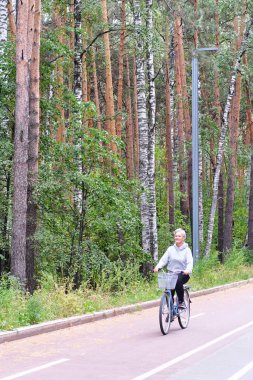 Aktif kıdemli beyaz saçlı kadın Forest Park 'taki bisiklet yolunda bisiklet sürüyor..