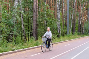 Aktif kıdemli beyaz saçlı kadın Forest Park 'ta bisiklet sürüyor. Yaşam tarzı kavramı.