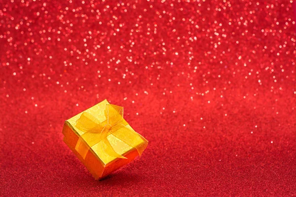 Una caja de regalo sobre un fondo de navidad borroso rojo — Foto de Stock
