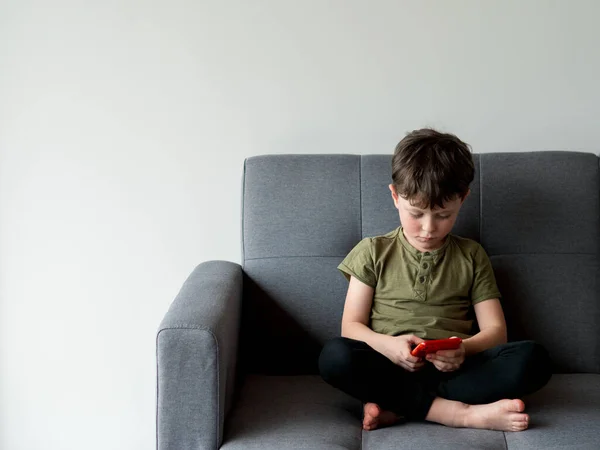 Little child with smart phone on sofa in room.