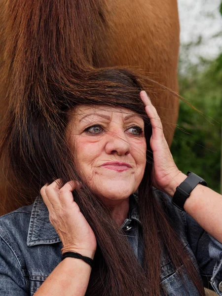 older woman putting on a horse's tail as a wig