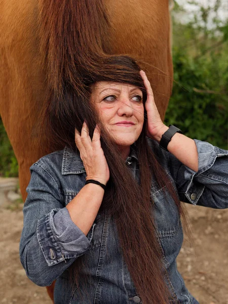 older woman putting on a horse\'s tail as a wig