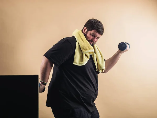 Obese man doing sports in an online class on the computer, with weights and towel
