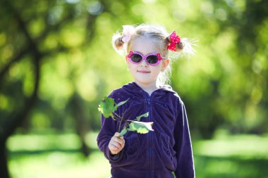 Saç stili çörekleri olan, güneş gözlüğü takan ve elinde yeşil ağaç dalı tutan etekli tatlı bir kız. Mutlu çocukluk, aşk bahar konsepti. Seçici odak.