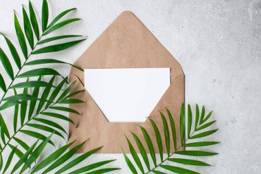 Gri beton arka planda boş ve yeşil yapraklı el işi zarf. Doğal organik ürünler kavramı. Üst görünüm, modelleme, kopyalama alanı. Reklam şablonu, davetiye kartı.