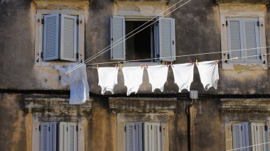 Yunanistan 'ın eski Corfu kentindeki binaların arasında asılı geleneksel kurutma çamaşırları. Çamaşır ipinde beş beyaz yelek. Seyahat kavramı.