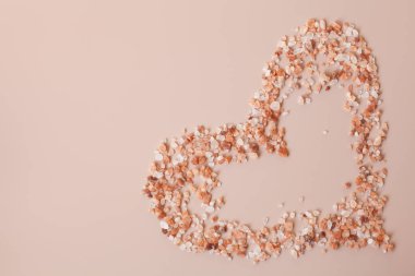 Eart şekilli pembe himalaya tuzu, toz pembe bir zemine saçılmış. Uzayı kopyala, üst görünüm. Sağlıklı yemek, vücut bakımı konsepti. 