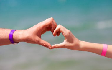 Mavi denizin arka planında kalp şeklinde erkek ve kadın elleri. Seyahat, turizm, ilişki ve mutluluk kavramı.