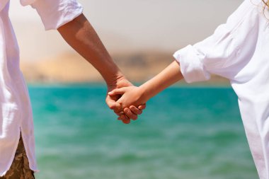 Mavi Kızıl Deniz ve Dağlar 'ın arka planında erkek ve kadın elleri birbirine yakın duruyor. Seyahat, turizm, ilişki ve mutluluk kavramı. Arka plan.