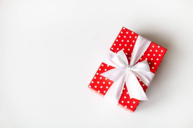 Kırmızı puantiyeli hediye paketi beyaz arka planda beyaz kurdeleli. Uzayı kopyala, üst görünüm. Tatil hediyesi, satış konsepti.