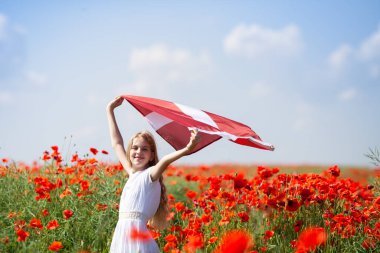 Gelincik tarlasında Letonya bayrağı tutan sarışın kız. Bağımsızlık Günü Bildirgesi. Ligo. Cumhuriyet Bildirgesi. Seyahat edin ve Letonca dil kavramını öğrenin.