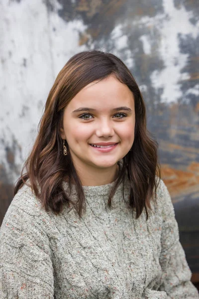 Junges Mädchen im beigen Pullover im Winter an einer städtischen Lagermauer sitzend — Stockfoto