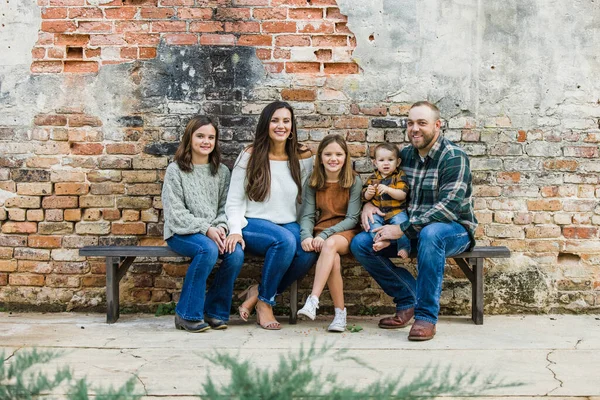 Familia mixta de cinco con dos niñas y un niño sentado en una mesa junto a una antigua pared de ladrillo urbano —  Fotos de Stock