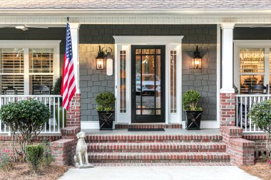 Ahşap, vinil kaplamalı ve büyük bir Amerikan bayrağı olan iki katlı mavi bir evin ön kapısı..