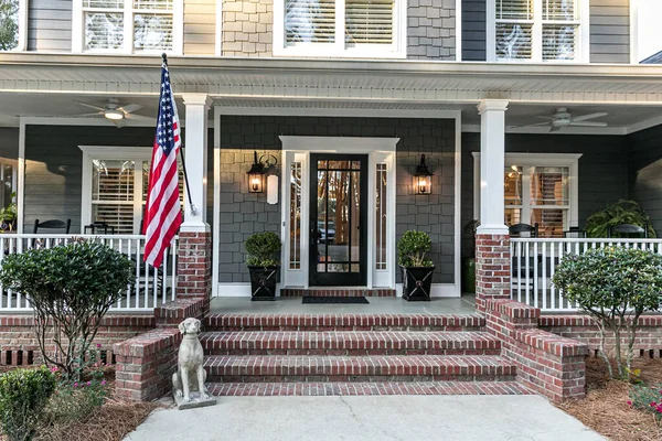 Front door entrance to a large two story blue gray house with wood and vinyl siding and a large American flag. — Stock Photo, Image