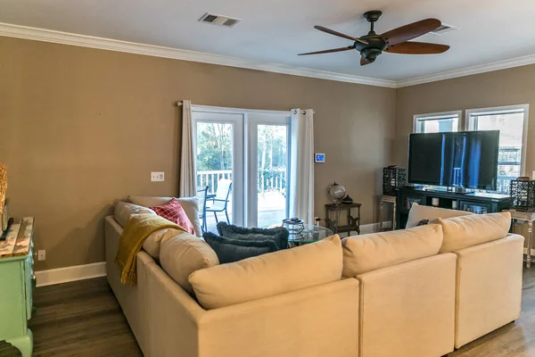 Lille stue med en cremefarvet sofa og et tv og en ventilator. - Stock-foto