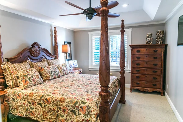 Маленькая главная спальня с большой деревянной кроватью с балдахином и старомодным цветочным комфортером с окном. — стоковое фото
