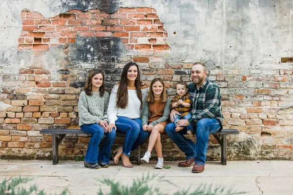 Familia mixta de cinco con dos niñas y un niño sentado en una mesa junto a una antigua pared de ladrillo urbano —  Fotos de Stock