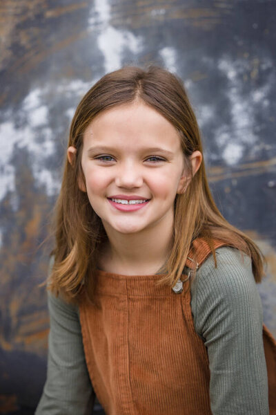 Young girl in a brown overall dress in the winter sitting near an urban warehouse wall