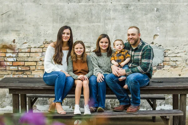 Смешанная семья из пяти человек с двумя девочками и маленьким мальчиком, сидящим на столе у старой городской кирпичной стены — стоковое фото