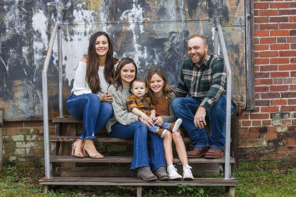 A family of five with two girls and a bbay boy sitting on the steps in a downtown urban location.