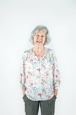 80 'lerinde mutlu, yaşlı bir kadın. Gri saçlı, beyaz bir arka planda tek başına duruyor.