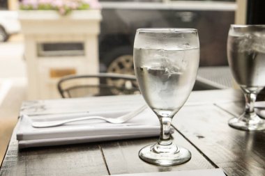 Bir su bardağı ve çatal bıçak takımı lüks bir restoranın ahşap masasında.