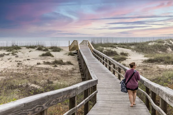 A woman walking alone on the wooden walkway path out to the ocean ar Tybee Island at Sunset. — Stock Photo, Image