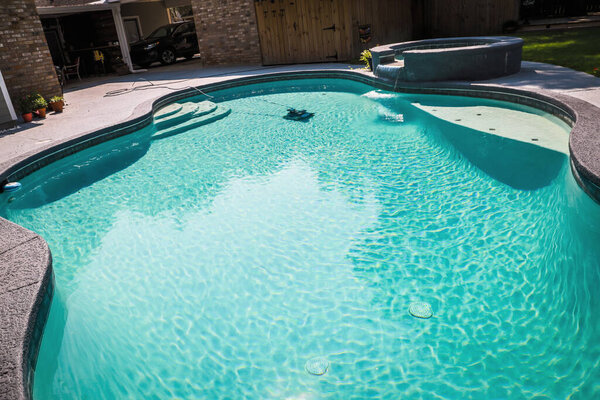 Большой серый бассейн свободной формы с бирюзовой голубой водой в огороженном дворе в пригороде.