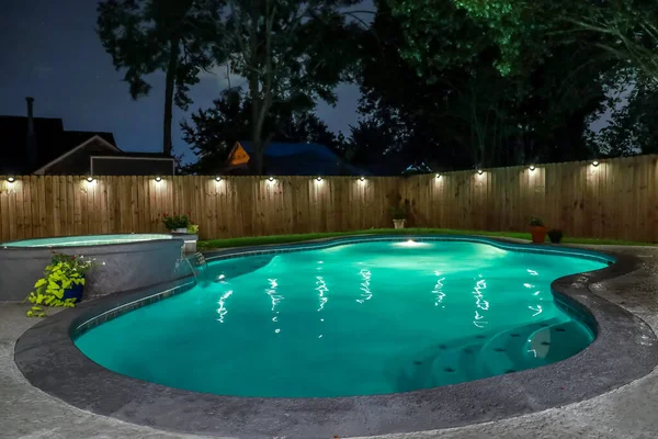 A backyard swimming pool and jacuzzi hot tob at night