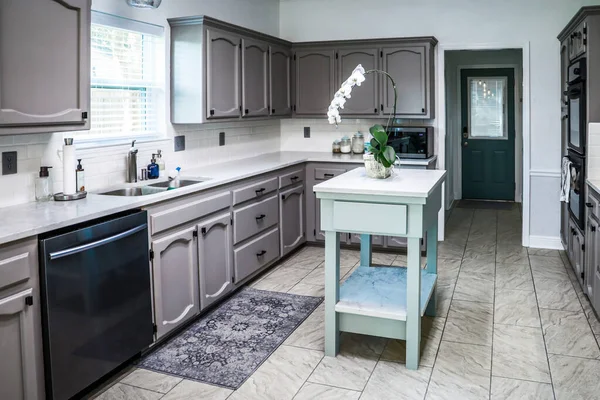 Una cocina renovada en una casa antigua con gabinetes grises pintados, encimeras de mármol, una pequeña isla portátil y un suelo de baldosas — Foto de Stock
