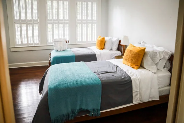 Спальня с двумя односпальными кроватями с бирюзовыми и серыми покрывалами и желтыми декоративными подушками — стоковое фото