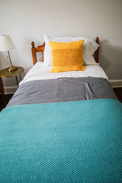 Гостевая спальня с односпальной кроватью с бирюзовым и серым покрывалом и желтой декоративной подушкой — стоковое фото