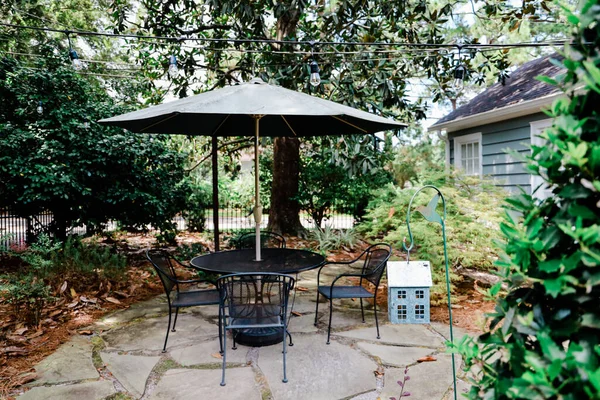 Patio trasero de una casa con una mesa de patio y unbrella y árboles — Foto de Stock