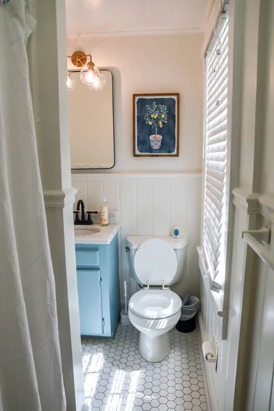 Ein kleines Gästebad mit einem Vintage-blauen Waschtisch, einem schwarzen Retro-Spiegel und einer Leuchte aus klarem Glas in einem kürzlich renovierten Ferienhaus — Stockfoto
