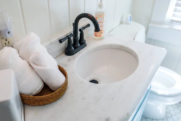 Un panier de serviettes blanches roulées propres organisées sur un comptoir de salle de bain dans une salle de bain d'invités près d'un lavabo et des toilettes. — Photo