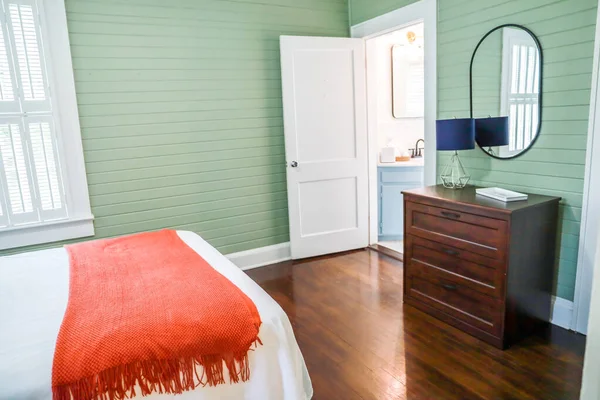 Proste ciemne drewno barwione komoda w sypialni gości z zielonym panelem ścian shiplap i czarnym obrączkowane lustro i mała lampa — Zdjęcie stockowe