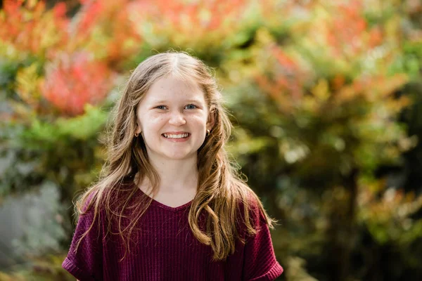 A waist up image of a young girl with long hair, freckles and a smile.