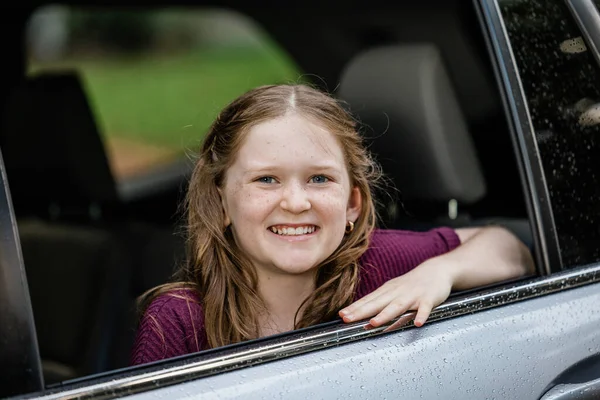 Little caucasian girl with freckles and a purple shirt looking out of a car window