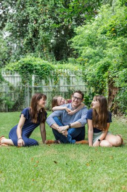 Anne ve babadan oluşan bir aile ve arka bahçelerinin çimlerinde oturan iki kız çocuğu ve en küçük kızı babalarına arkadan sarılıyorlar.