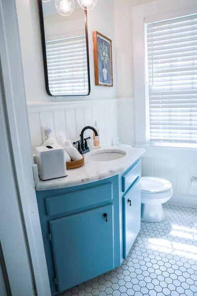 A small guest bathroom with a vintage blue vanity, retro black mirror, and clear glass light fixture in a recently renovated short term rental cottage — Stock Photo, Image