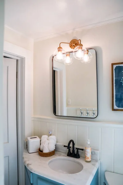 A small guest bathroom with a vintage blue vanity, retro black mirror, and clear glass light fixture in a recently renovated short term rental cottage — Stock Photo, Image