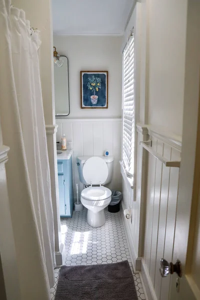 Ein kleines Gästebad mit einem Vintage-blauen Waschtisch, einem schwarzen Retro-Spiegel und einer Leuchte aus klarem Glas in einem kürzlich renovierten Ferienhaus — Stockfoto