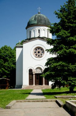 Güneşli bir günde haç ve yuvarlak pencereli beyaz ortodoks kilisesine giden yol ve Sırbistan 'ın Sokobanja kentinin merkezinde mavi gökyüzü 
