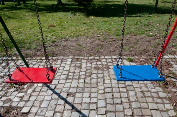 Parkta iki metal, kırmızı ve mavi boş salıncak.